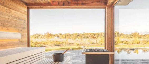 Modernes Interieur einer Sauna mit Holzverkleidung, Blick auf eine grüne Landschaft und einen Teich draußen.