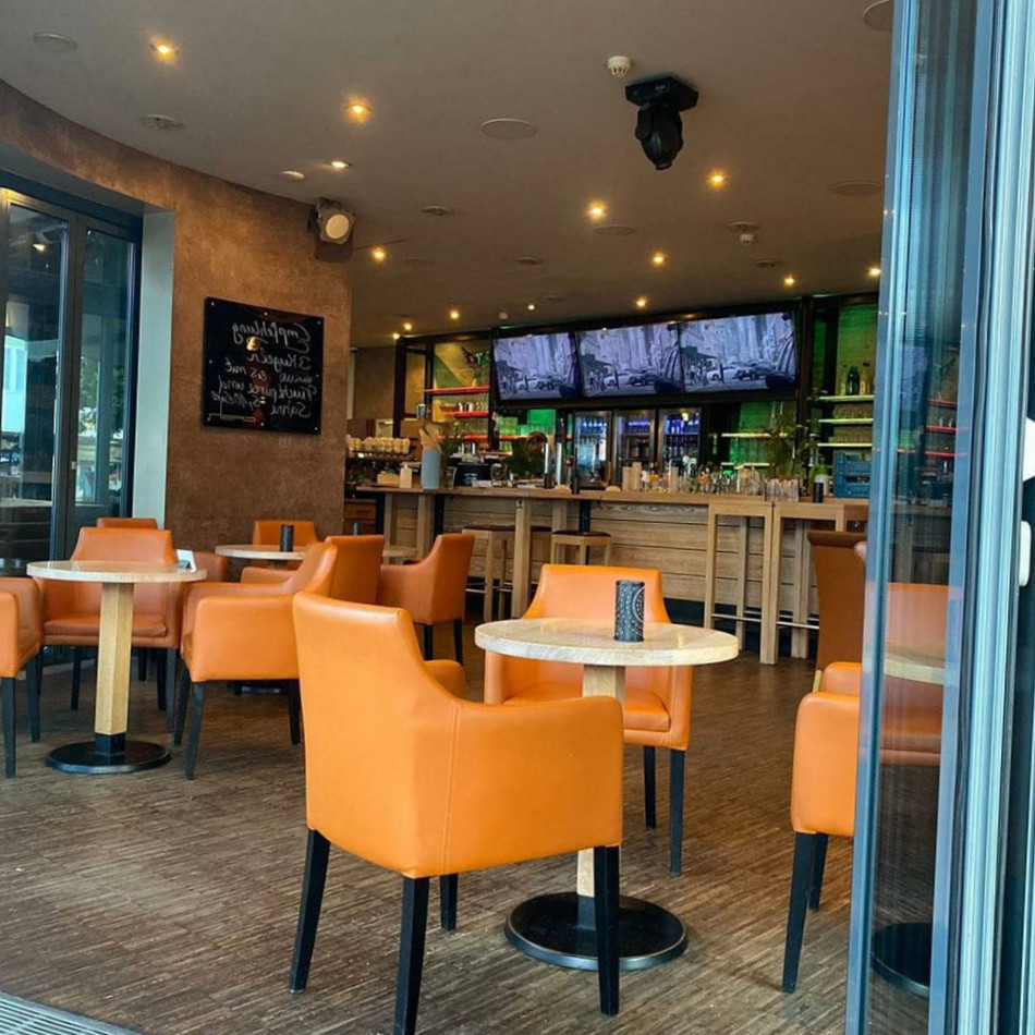 Gemütliches Café mit orangefarbenen Stühlen, Tischen und einer Bar im Hintergrund mit Fernsehern und einer Getränkeaus...