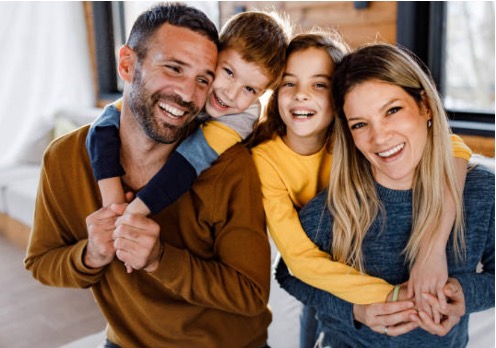 Ein glückliches Familienporträt mit einem Paar und zwei Kindern, die zusammen lachen und sich umarmen.
