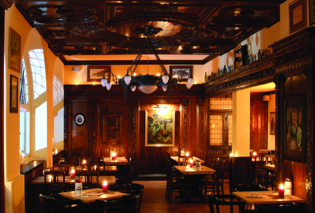 Gemütliches Restaurant mit Holzmöbeln, Kerzenlicht und kunstvollen Verzierungen an Wänden und Decke.