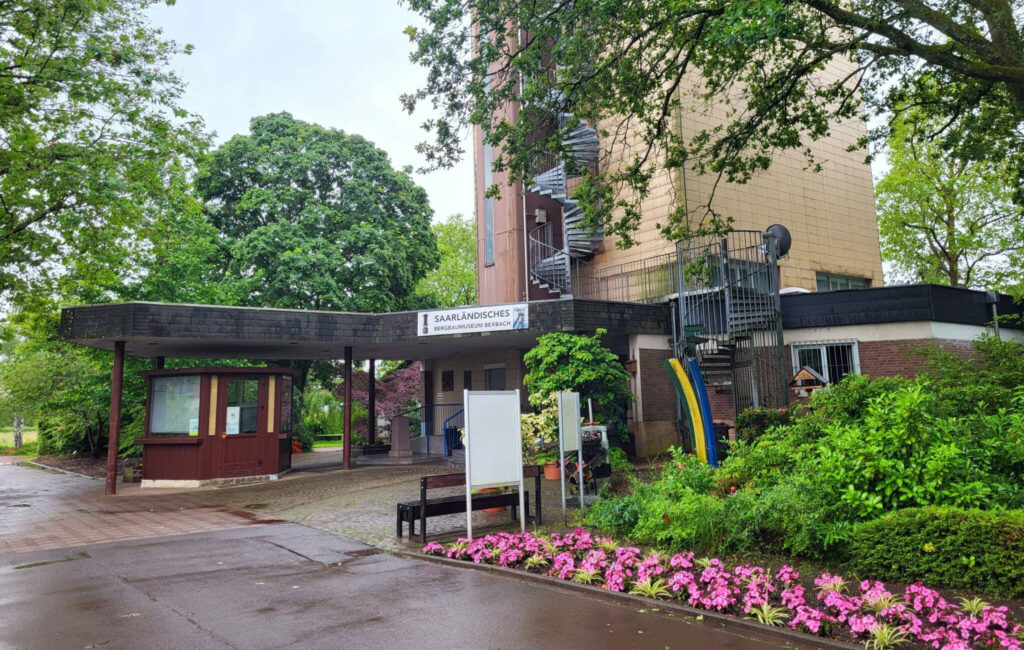 Eingang zum Saarländischen Bergbaumuseum in Bexbach, umgeben von Grünflächen und bunten Blumen.