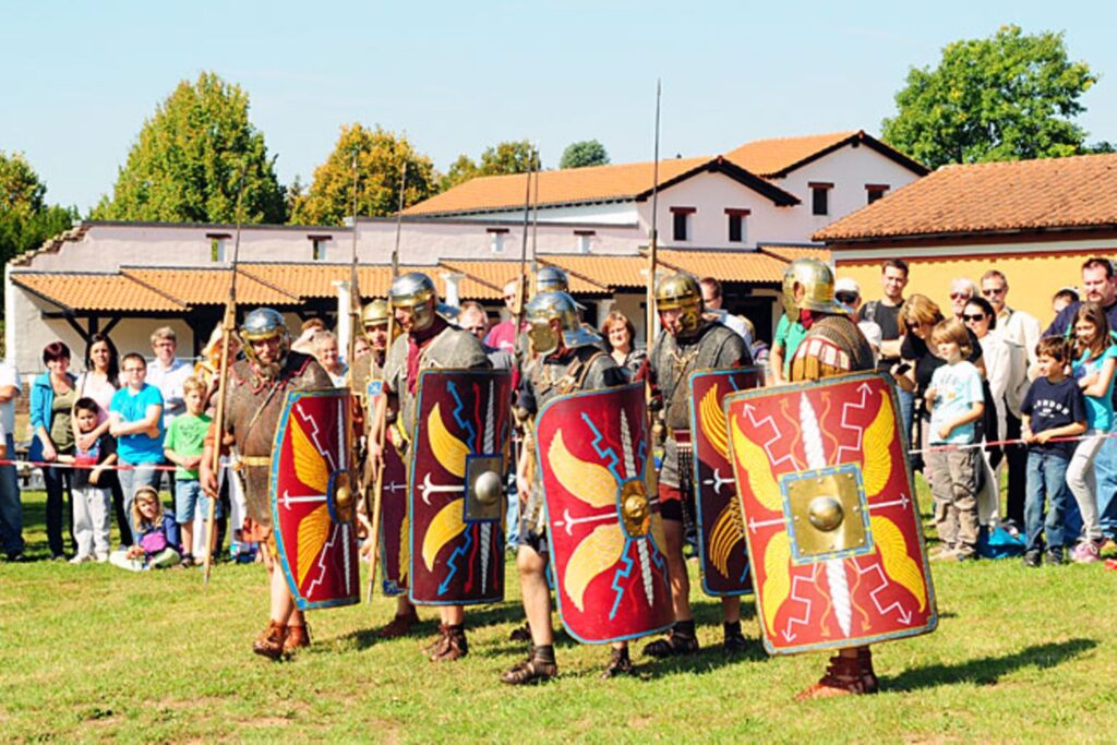 Römische Soldaten in historischer Kleidung marschieren vor einer Zuschauermenge in einer Freiluftveranstaltung.