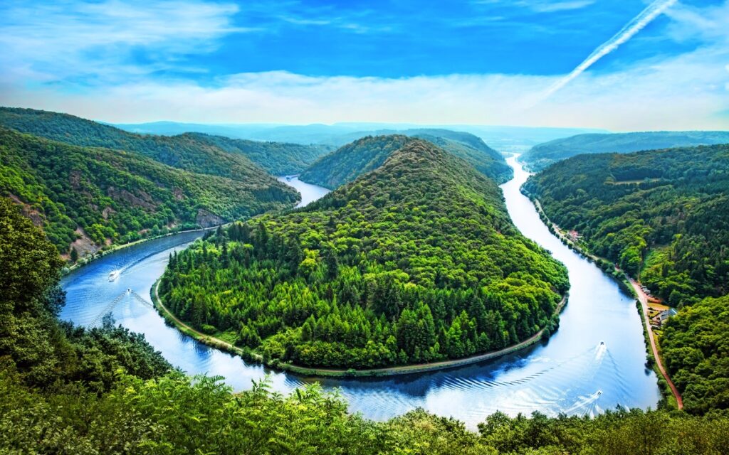 Aussicht auf einen gewundenen Fluss, umgeben von grünen Hügeln und Bäumen, unter blauem Himmel mit Wolken.