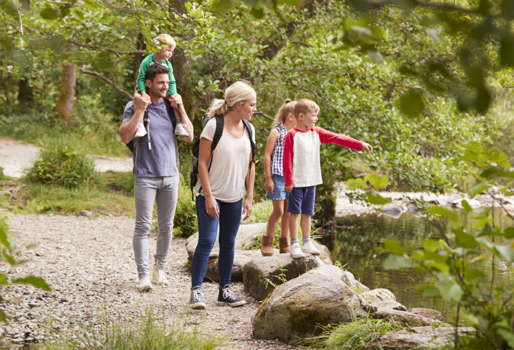 Familie macht einen Spaziergang am Ufer eines Gewässers und beobachtet die Natur. Kinder stehen auf Steinen.